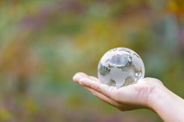 Human hand holding globe planet glass In green forest with bokeh nature lights. world environment...