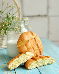 Bun of wheat flour on wooden table with jug of milk and wicker basket in background. Still life.