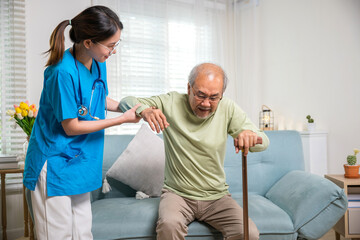 Caring nurse helping supporting senior disabled man to stand up with walking stick, young woman...
