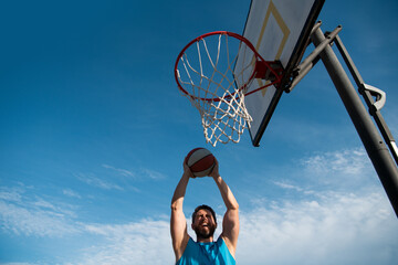 Basketball player making a jump shot against blue sky background.