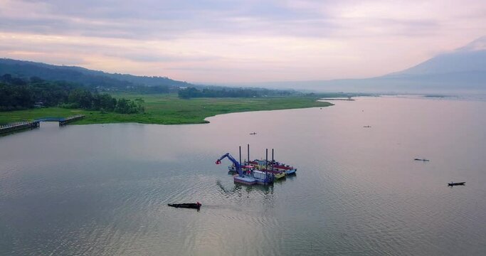 Drone shot of Dredger boat with excavator on the lake with mountain on the background - Rawa Pening Lake, Indonesia
