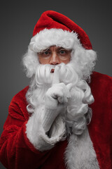 Shot of isolated on grey santa claus posing with finger at his lips.