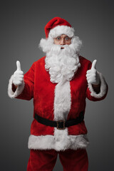 Portrait of isolated on grey santa claus with thumbs up dressed in red suit and hat.