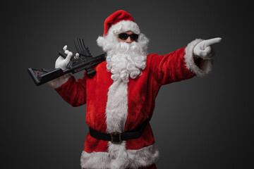 Shot of cool santa holding rifle on his shoulder pointing his finger away.