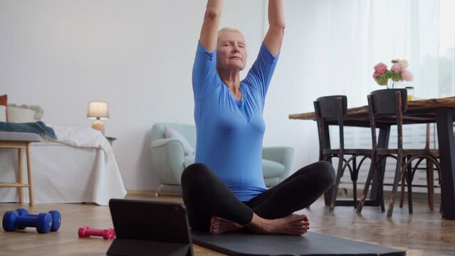 elderly woman sitting in a yoga pose in front of an open laptop.