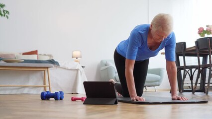elderly woman doing exercises with an online trainer in her living room.