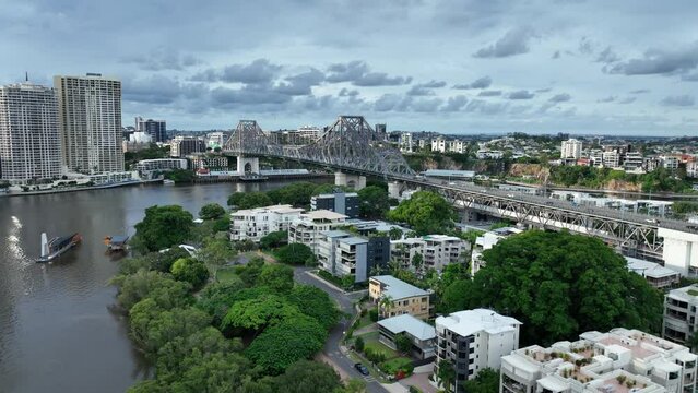Drone orbiting shot of Brisbane's Story Bridge a heritage-listed steel cantilever bridge. Shot from above Brisbane River near Captain Burke Park. Cloudy Sky 4K