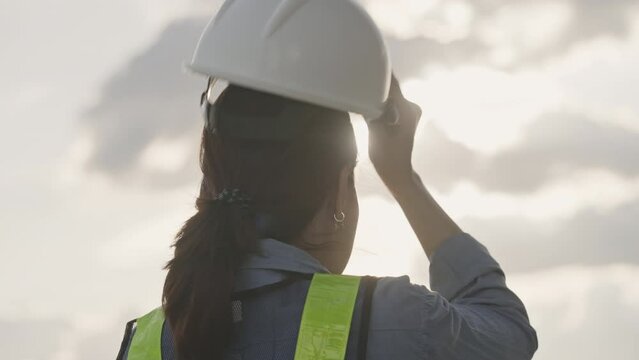 Slow motion of a female engineer talking off a construction helmet on at sunset,Finish working,Engineering Concept,Close-up
