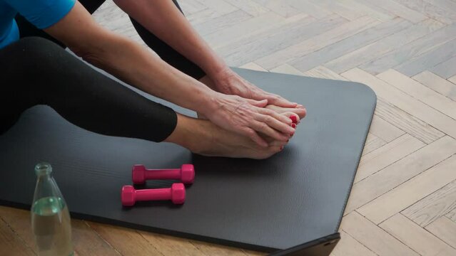 elderly woman with dumbbells sitting on a sports mat.