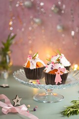 Cupcakes with white icing, pink and purple sprinkles on a glass stand in New Year's decor on a green plain background. New Year's desserts.