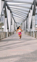 Cheerful woman runner running across a city bridge. Wellness concept.
