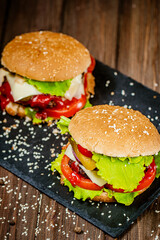 Top down view of delicious burgers with beef, cheese, tomato, lettuce on board. Selective focus
