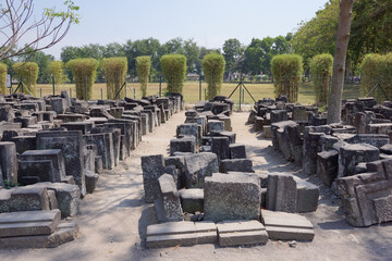 View of row of unidentified stone blocks from ancient hindu Prambanan Temple ruin complex with trees and sunny clear blue sky background. No people.
