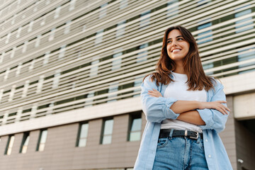 Portrait confident young woman standing in the city looking to the side with happy expression