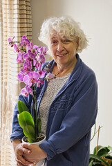 Senior woman holding a lilac orchid and smiling at the camera.