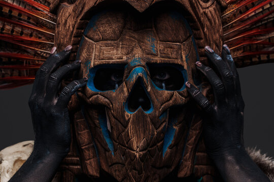 Headshot of isolated on grey aztec witch with mask looking at camera.