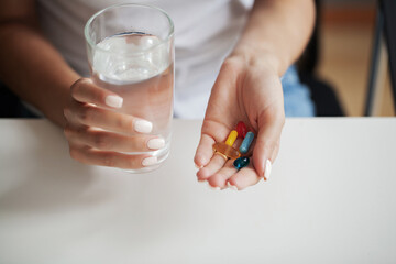 Young woman takes round pill with glass of water in hand