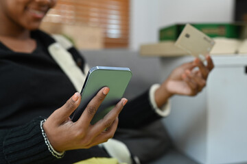 Cropped shot of smiling woman holding credit card, making payment on internet via mobile phone