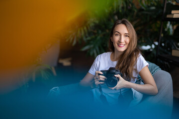 a girl photographer with a camera smiles while sitting in a chair with many books.