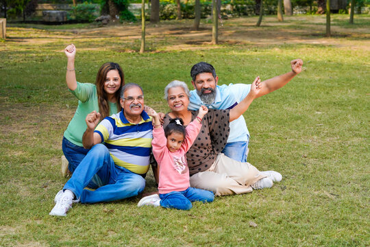 Happy Indian Or Asian Family Sitting At Park.