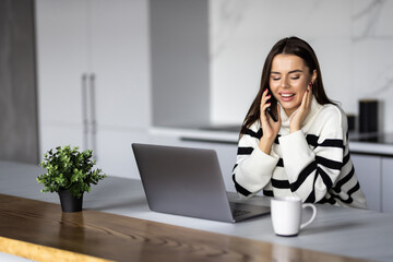 Beautiful woman drinking coffee and talk phone in the kitchen. Young woman talking to the phone.