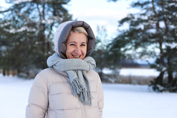 Obraz premium Portrait of happy beautiful elderly senior retired woman in age is playing, having fun with snow outdoors in forest or park at winter cold day, smiling, enjoy weather