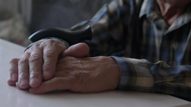 close-up of an old man's hand on a table and a walking stick..selective focus.a pensioner reflects on the past, nostalgia of an elderly person