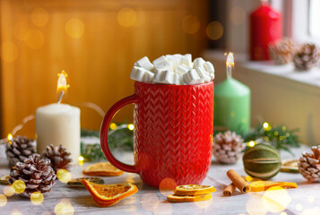 close-up of a red cup with white marshmallows on the table next to pine cones, lemon and candles. winter holidays, Christmas, New Year