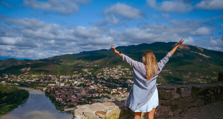 Young woman blonde tourist posing arms outstretched, confluence of two rivers Aragvi and Kura,...