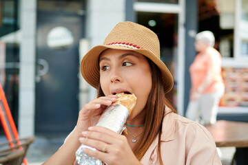 A beautiful Hispanic female in a hat eating a kebab in a cafe on a sunny day