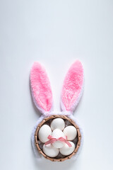 Top view of basket with white Easter eggs and Easter bunny ears on white background, copy space for...