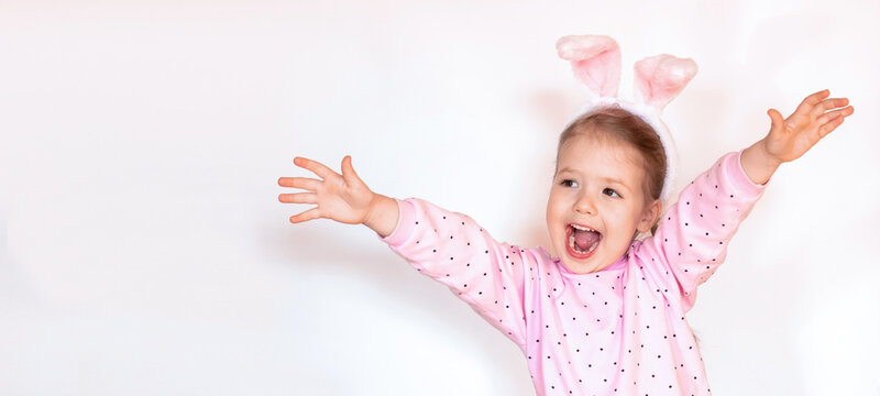 girl with hands up. Cute smiling happy child in pink jacket with Easter bunny ears on white background, copy space