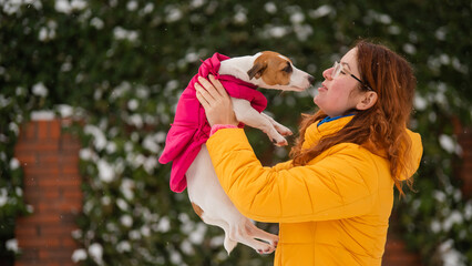 Caucasian woman hugging with dog while walking in winter. Jack Russell Terrier in a warm pink jacket.