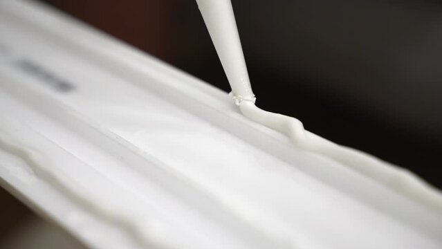 Dolly shot of zig zag glue applying on white baseboard surface with industrial tube, white sealant for plinth installing on construction site, using adhesive materials for home improvements
