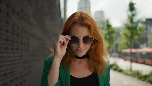 Young stylish redhead woman standing in the city with sunglasses and cup of coffee.