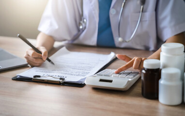 Fototapeta premium Doctor physician with stethoscope calculate medical fee costs & revenue. practitioner use calculator at Clinic.