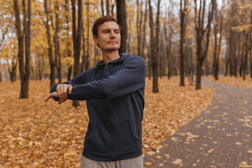 Athletic male jogger stretching and warming up while exercising during fitness training in autumn park 