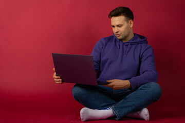 young man in purple hoodie talking on video call with laptop on red background
