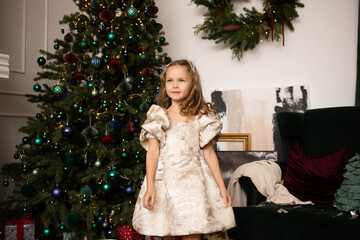 Little happy girl in dress standing near Christmas tree at home