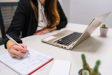 Cropped image of hands of young entrepreneur girl working with her laptop writing things down with...
