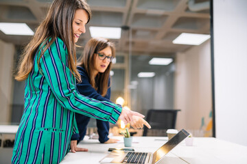 Young executive girl in an American jacket attending to her client and pointing to her laptop screen. Entrepreneur woman.
