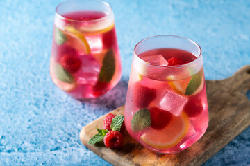 Raspberry lemonade drink in glass on blue background