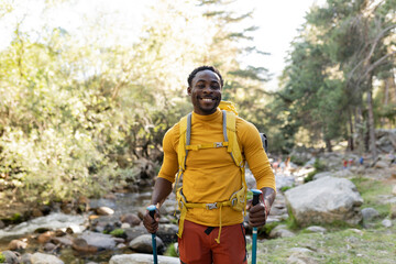 Cheerful middle age African American man trekking outdoors in the forest on a sunny day - Adventure...