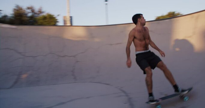 Authentic and fit shirtless skater ride inside bowl on warm summer evening, practice tricks on skateboard. Skater ride with flow in pool. Skateboarding as sport concept