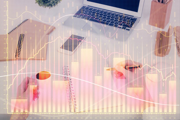 Hands writing information about stock market in notepad. Forex chart holograms in front. Concept of...