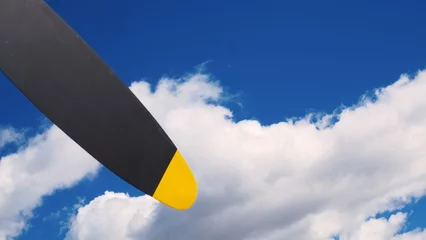 Poster Yellow helicopter circles in distance in blue sky with clouds. Gray propeller blades turn slowly as helicopter flies back and forth in sky and is about to land. Gray blades with yellow stripes at ends © ShantiMedia
