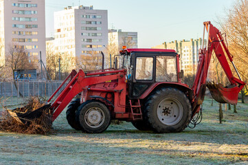 A red tractor picks up branches in a bucket. Cleaning in the park