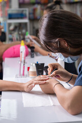 Vertical photo of a professional manicurist applying a clear base coat to a woman's nails.