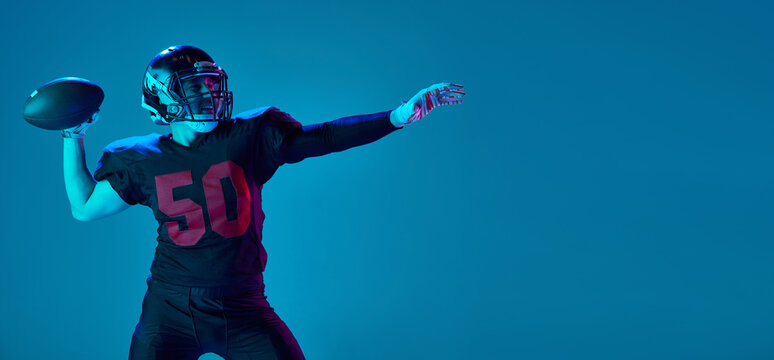 Strong throw. Professional american football player in sports team uniform and protective helmet isolated over blue background in neon light. Power, energy, achievements, skills