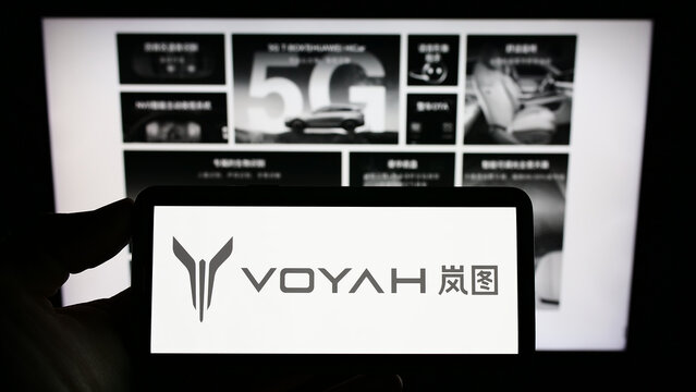 Stuttgart, Germany - 12-03-2022: Person holding mobile phone with logo of Chinese luxury car manufacturer Voyah on screen in front of company web page. Focus on phone display.